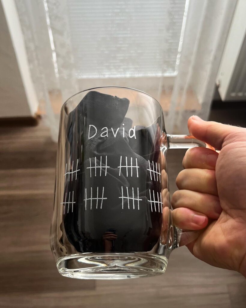 a hand holding a glass mug with a number written on it