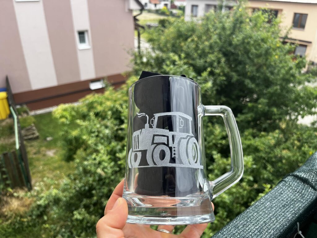 a hand holding a glass mug with a tractor design